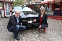 Vor den rot weißen Losbuden steht der schwarze Mercedes, davor hocken links Dietmar Hoppe von der  Bürgerpark-Tombola, rechts Simone Schnase, die Gewinnerin des Mercedes. Symbolisch halten beide einen großen Schlüssel in der Hand. Das Foto wurde von Martin Rospek gemacht.